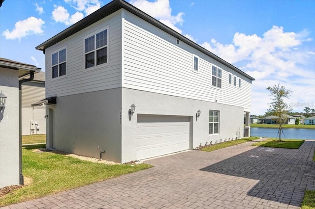 view of side of home featuring decorative driveway, a garage, a water view, and stucco siding