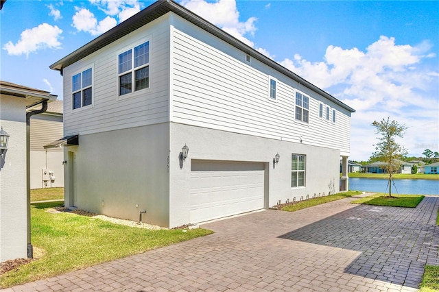 view of side of property with stucco siding, an attached garage, decorative driveway, and a water view