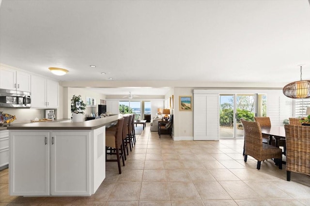 kitchen with dark countertops, white cabinets, stainless steel microwave, and light tile patterned flooring