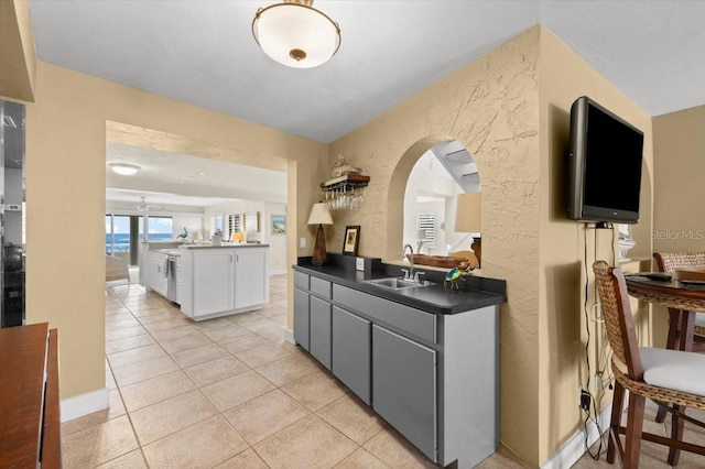 kitchen with a textured wall, dark countertops, white cabinetry, a sink, and light tile patterned flooring