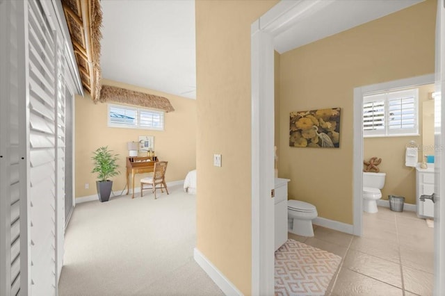 hallway featuring light colored carpet, baseboards, and light tile patterned floors