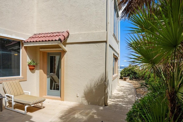 view of side of home with a tile roof, a patio, and stucco siding