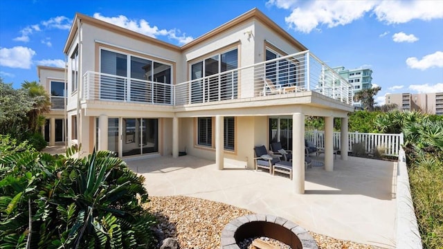 rear view of house with an outdoor fire pit, a balcony, fence, a patio area, and stucco siding