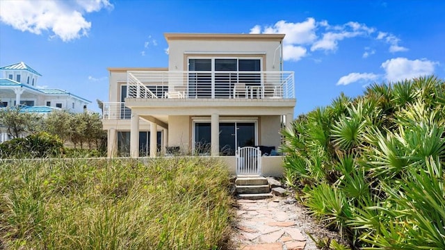 rear view of property featuring a gate, fence, a balcony, and stucco siding