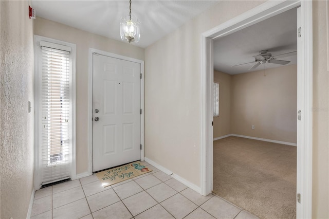 foyer featuring ceiling fan with notable chandelier, light colored carpet, baseboards, and light tile patterned floors