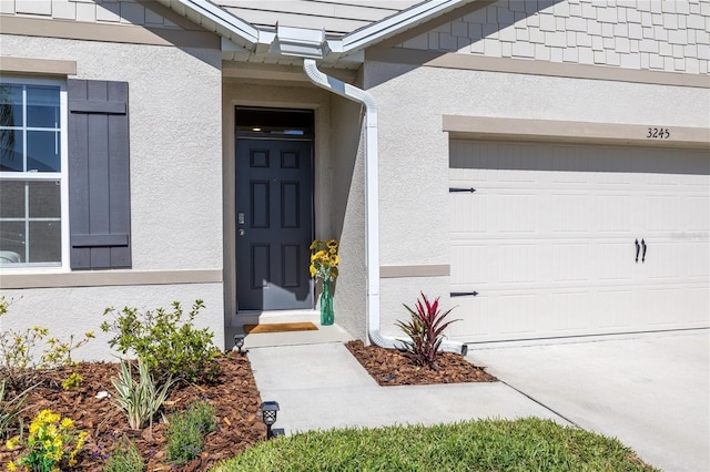 view of exterior entry with a garage and stucco siding