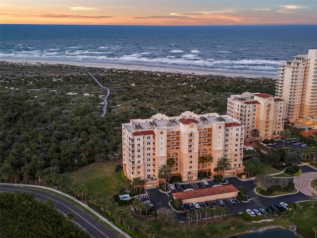 aerial view at dusk featuring a water view and a view of the beach