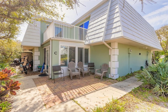 back of property with a balcony, a patio area, mansard roof, and stucco siding