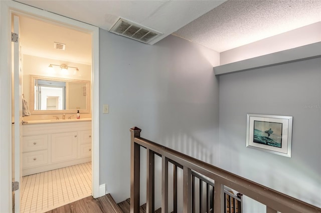 corridor with a textured ceiling, an upstairs landing, a sink, and visible vents