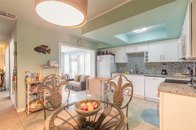 kitchen featuring white appliances, a raised ceiling, decorative backsplash, and light tile patterned flooring