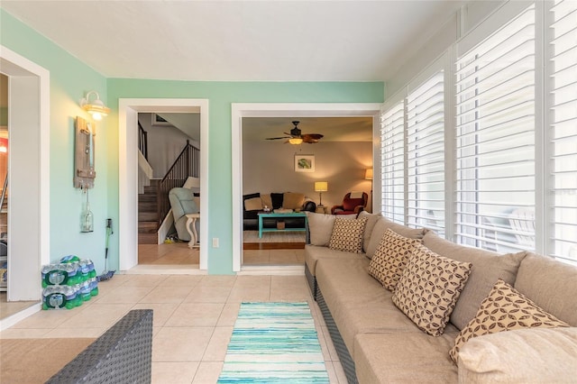 living area with light tile patterned floors, ceiling fan, and stairs