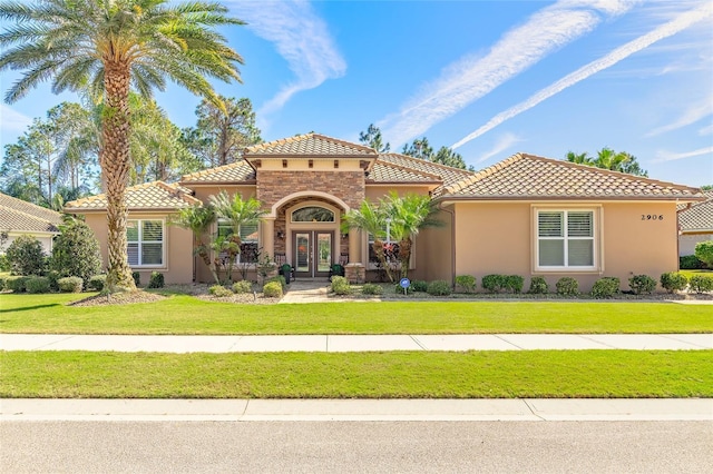 mediterranean / spanish-style home with a tiled roof, french doors, a front lawn, and stucco siding