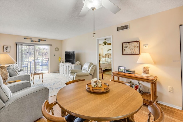 living area featuring baseboards, visible vents, a ceiling fan, light wood-style flooring, and a textured ceiling