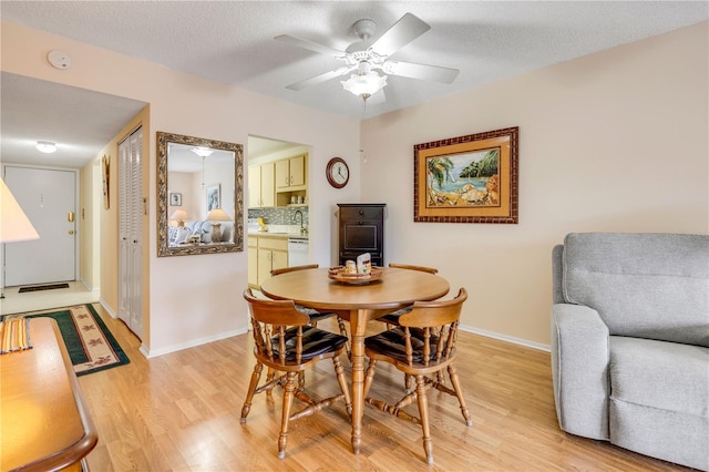 dining room featuring a textured ceiling, light wood finished floors, a ceiling fan, and baseboards