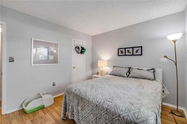 bedroom with a textured ceiling, baseboards, and wood finished floors