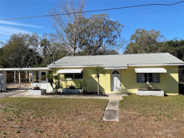 view of front of house with a shingled roof, a front yard, and concrete block siding