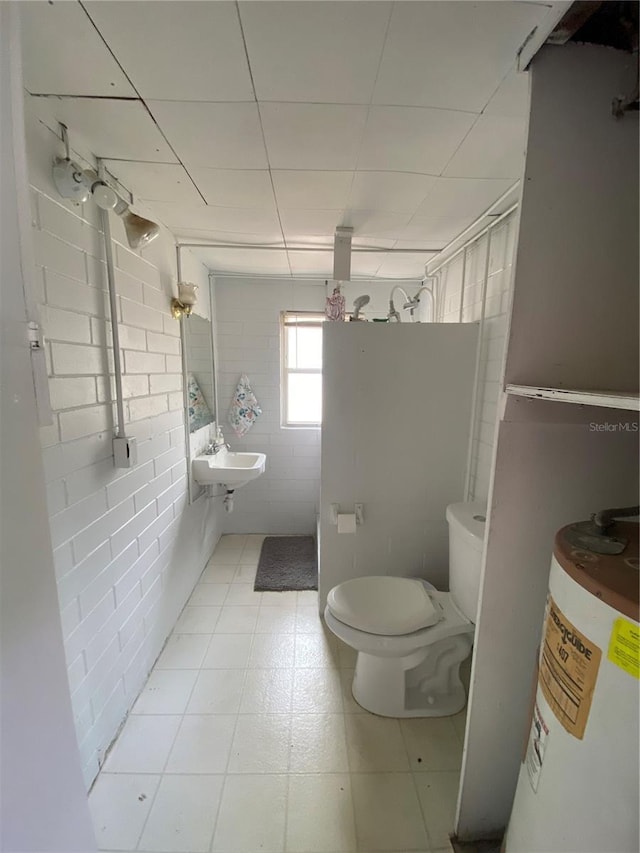 bathroom with toilet, a sink, electric water heater, and tile walls