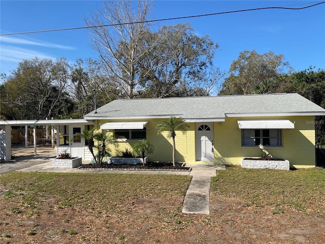 view of front facade with concrete block siding, a front lawn, an attached carport, and roof with shingles
