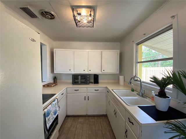 kitchen with light countertops, freestanding refrigerator, visible vents, oven, and a sink