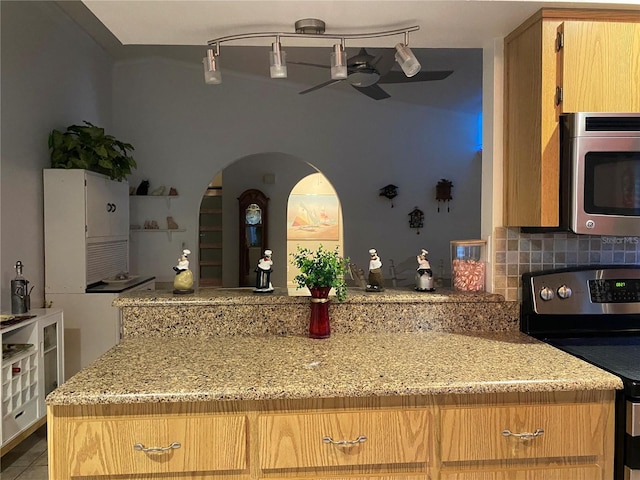 kitchen featuring light stone counters, arched walkways, ceiling fan, stainless steel appliances, and backsplash