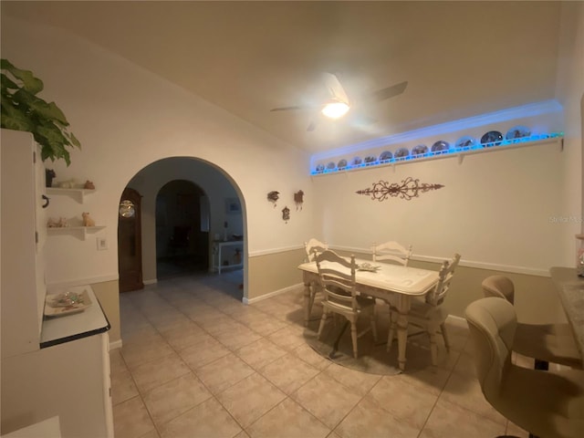 dining area featuring baseboards, arched walkways, light tile patterned flooring, and a ceiling fan