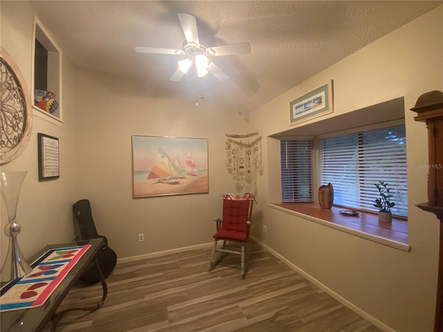 living area featuring baseboards, a textured ceiling, wood finished floors, and a ceiling fan