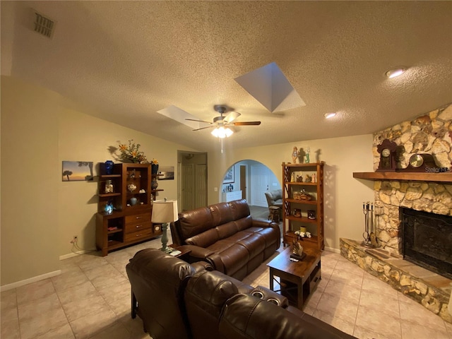 living area featuring a stone fireplace, a skylight, a ceiling fan, and visible vents