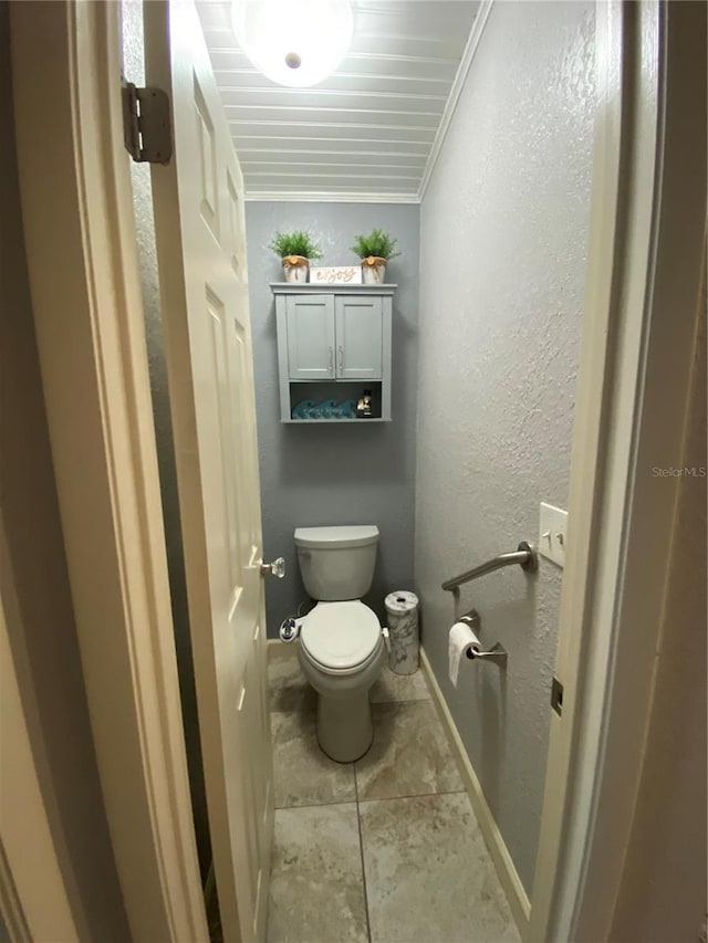 bathroom with baseboards, ornamental molding, tile patterned flooring, toilet, and a textured wall