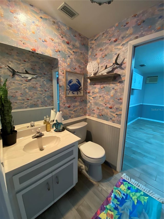 bathroom featuring visible vents, toilet, wainscoting, wallpapered walls, and vanity