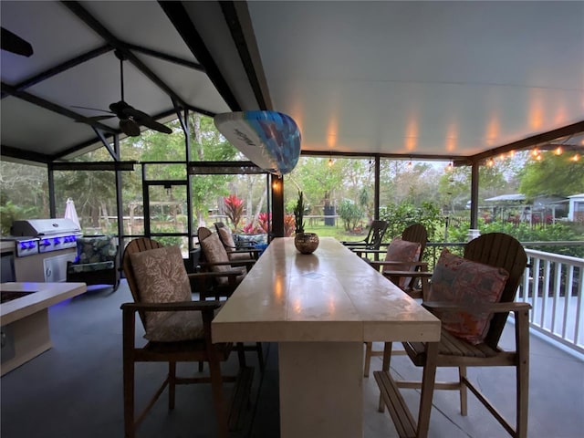 sunroom / solarium featuring a healthy amount of sunlight, vaulted ceiling with beams, and a ceiling fan