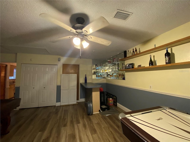 playroom featuring visible vents, a ceiling fan, a textured ceiling, dark wood-style floors, and a dry bar