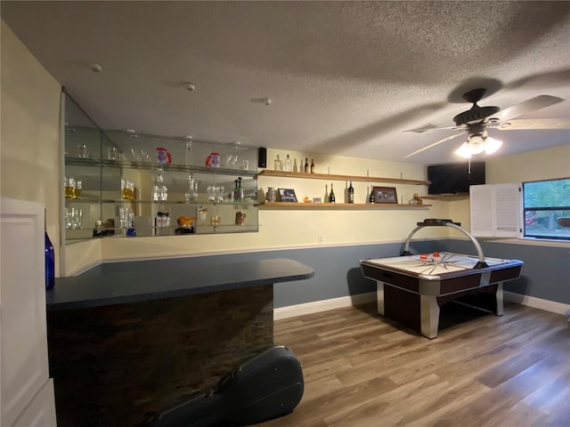 game room with a ceiling fan, a textured ceiling, wood finished floors, a bar, and baseboards