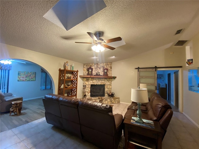 living area with visible vents, a stone fireplace, a textured ceiling, tile patterned floors, and ceiling fan with notable chandelier