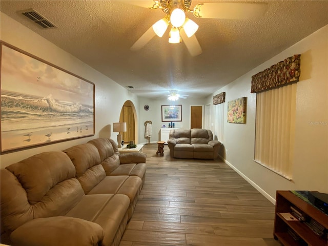 living area with visible vents, hardwood / wood-style floors, arched walkways, a textured ceiling, and a ceiling fan