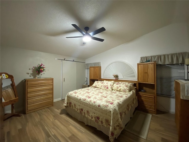 bedroom featuring a textured ceiling, a ceiling fan, light wood-style floors, and vaulted ceiling