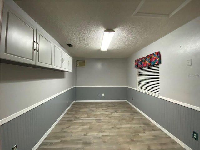 unfurnished room featuring visible vents, light wood-style flooring, a textured ceiling, and a wainscoted wall