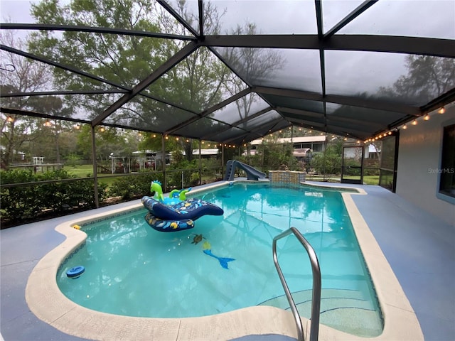 pool featuring glass enclosure, a water slide, and a patio