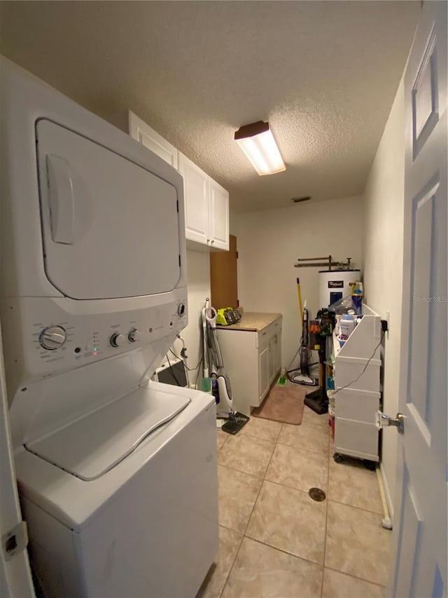 laundry room featuring light tile patterned floors, cabinet space, a textured ceiling, and stacked washer and dryer