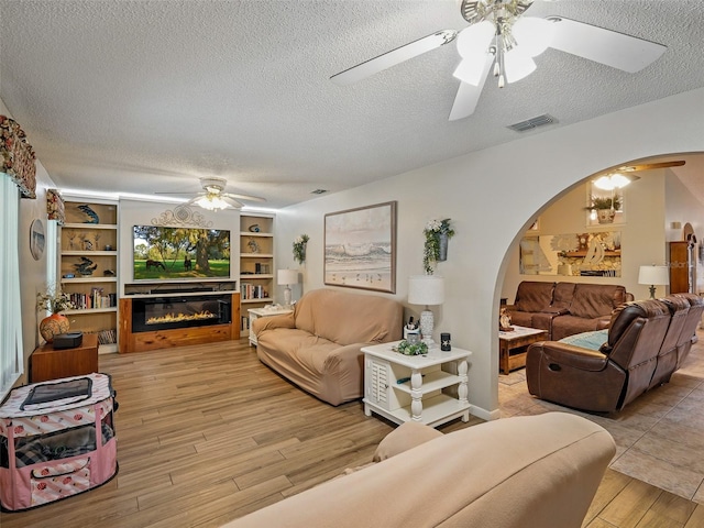 1370 Jane Lacey Ln, New Smyrna Beach, FL 32168 - living area featuring arched walkways, ceiling fan, wood finished floors, a glass covered fireplace, and a textured ceiling