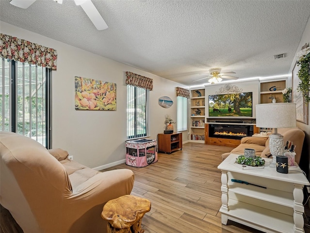 1370 Jane Lacey Ln, New Smyrna Beach, FL 32168 - living area with ceiling fan, a textured ceiling, light wood-style flooring, a glass covered fireplace, and baseboards
