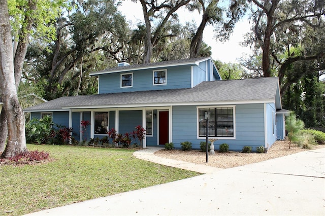 traditional home featuring a shingled roof, a porch, a chimney, and a front lawn