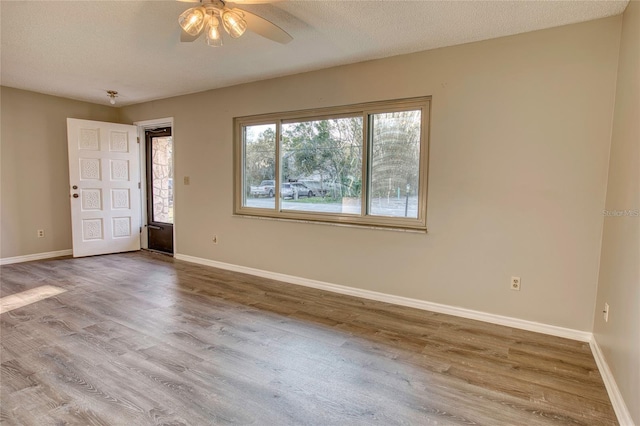 unfurnished room with a textured ceiling, wood finished floors, a ceiling fan, and baseboards