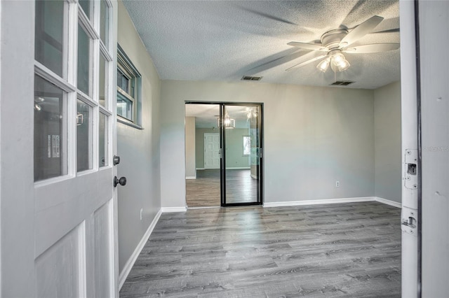 spare room featuring a textured ceiling, wood finished floors, visible vents, and a ceiling fan