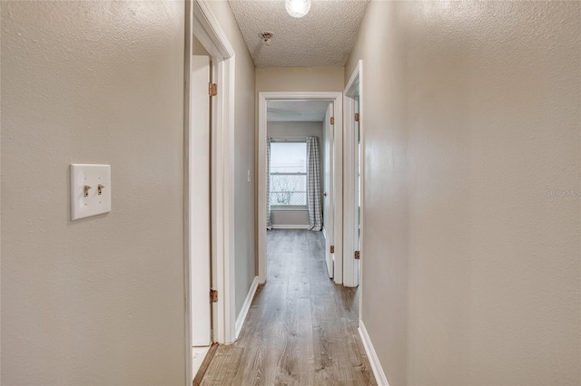 hall featuring light wood-type flooring, baseboards, and a textured ceiling