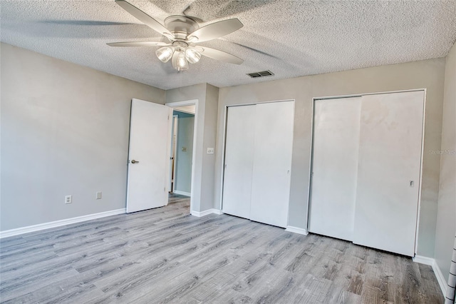 unfurnished bedroom with multiple closets, visible vents, a textured ceiling, and wood finished floors