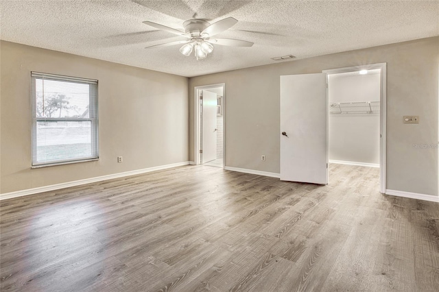 unfurnished bedroom with light wood-type flooring, a walk in closet, visible vents, and baseboards