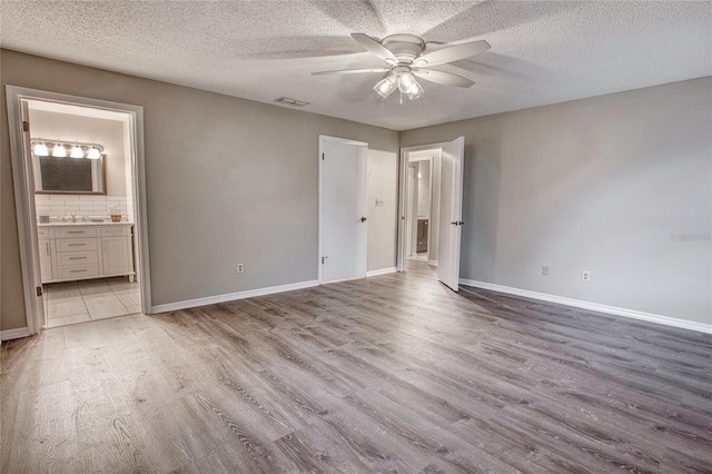 unfurnished bedroom featuring baseboards, visible vents, ensuite bath, wood finished floors, and a textured ceiling