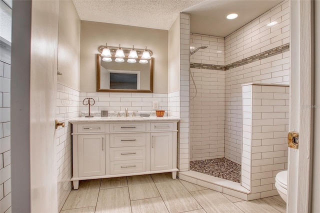 bathroom featuring a textured ceiling, toilet, vanity, tile walls, and a tile shower