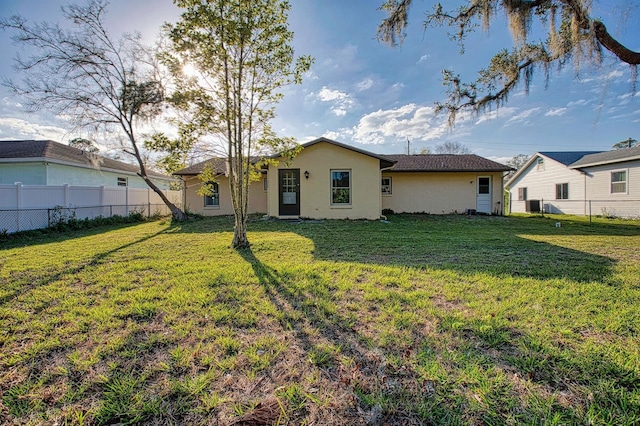 back of property featuring fence, a lawn, and stucco siding