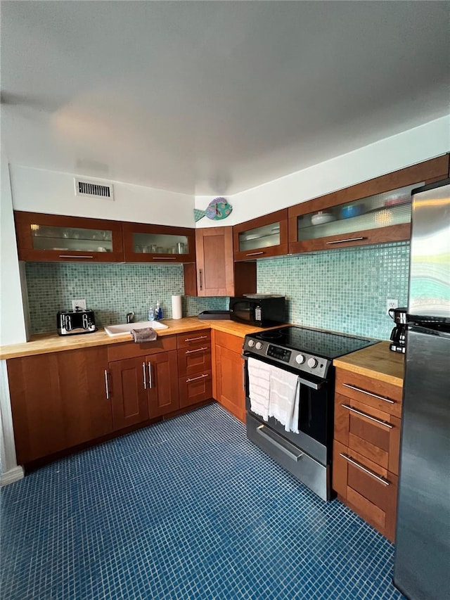 kitchen with butcher block countertops, glass insert cabinets, appliances with stainless steel finishes, a sink, and backsplash